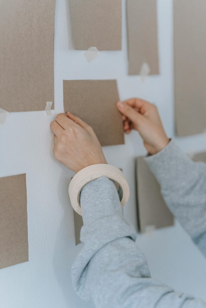 Person in Gray Long Sleeve Shirt Holding A Cardboard On Wall